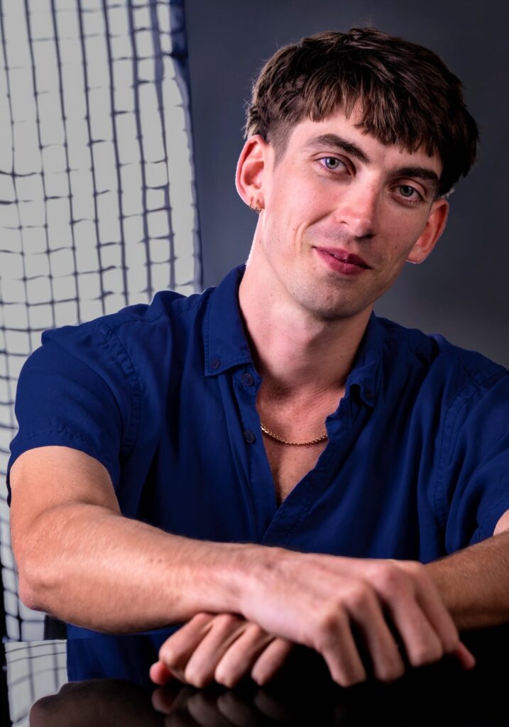 Sam sitting down, wearing blue shirt, staring at camera, with arms partially crossed