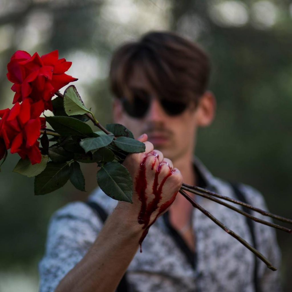 Sam grasping thorny roses, with blood dripping down hand